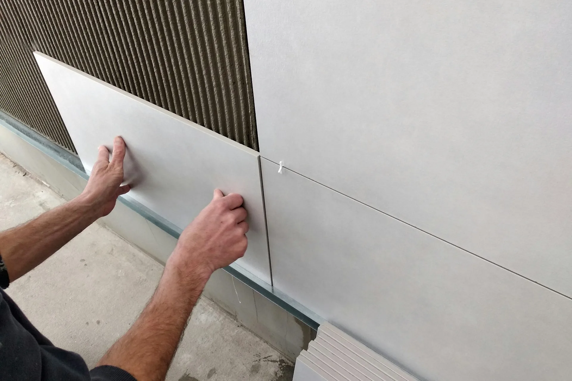 Hands pressing a large grey tile onto an adhesive-covered wall